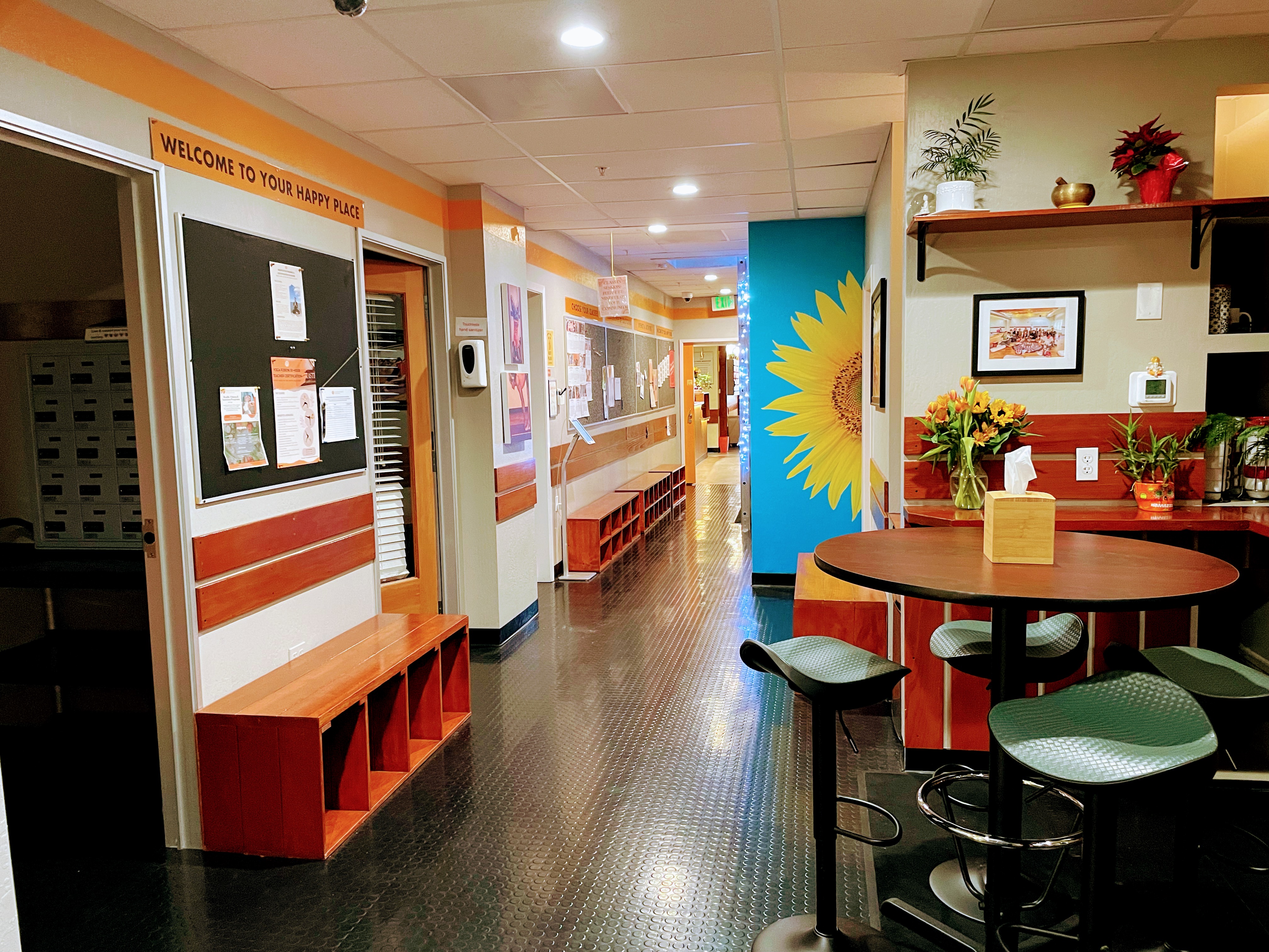 Studio 3 lobby with a round table, green chairs and a sunflower mural